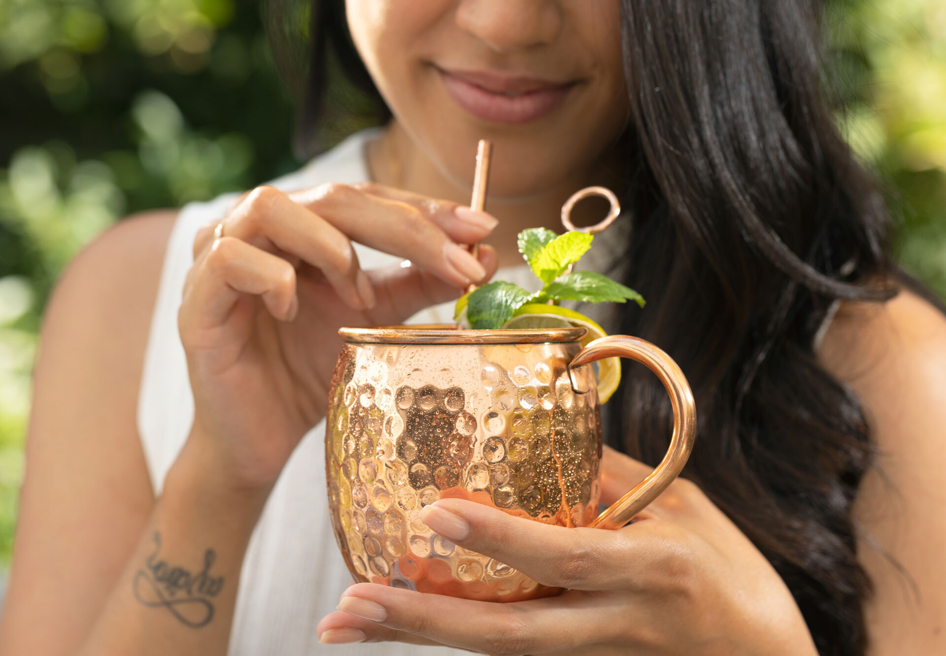 Frau hält einen Kupferbecher mit Cocktail, Strohhalm und Zitronenscheibe. Grüner Hintergrund.