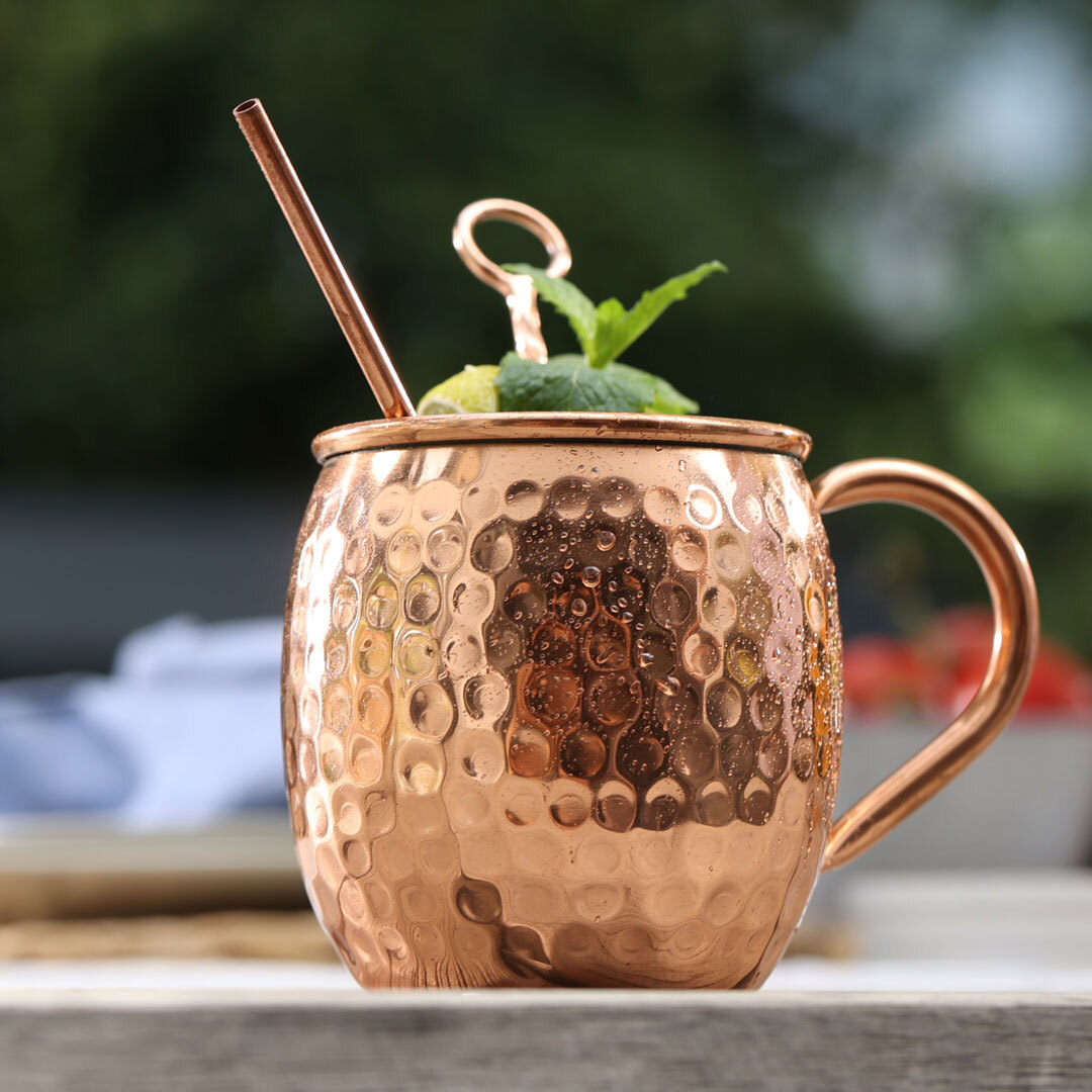 Ein kupferfarbener Becher mit Getränk, Strohhalm und Minze. Bokeh-Hintergrund.