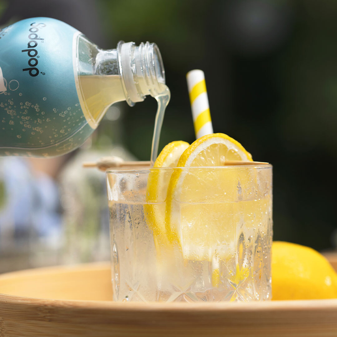 Limonade wird in ein Glas mit Zitronenscheiben und einem Strohhalm auf einem Holztablett gegossen.