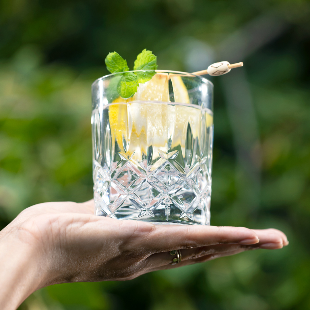 Eine Hand, die ein Kristallglas mit einem Cocktail aus Zitronenscheiben und Minzblättern hält.