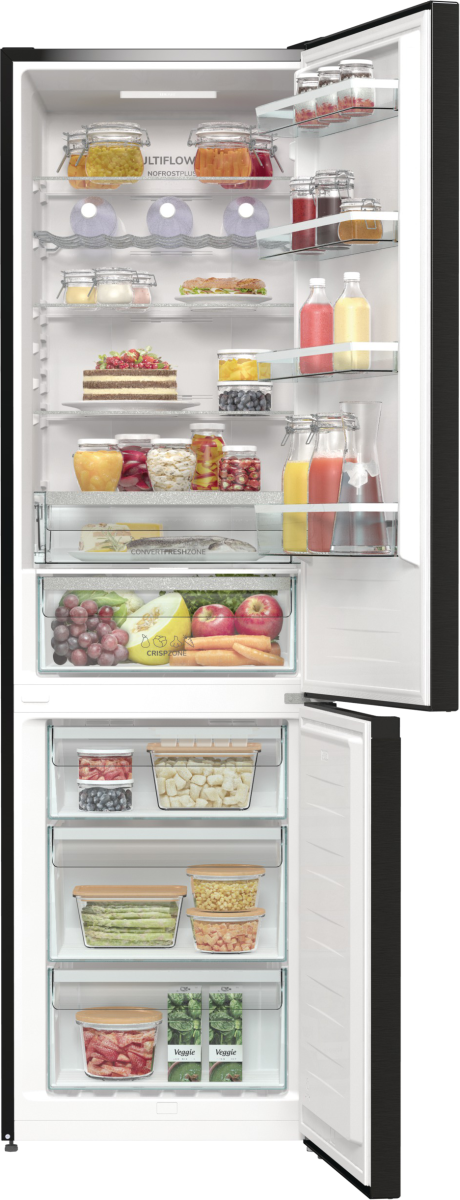 Otwarta lodówka z jedzeniem i napojami. Widoczne szklane półki, owoce, warzywa, słoiki i butelki.