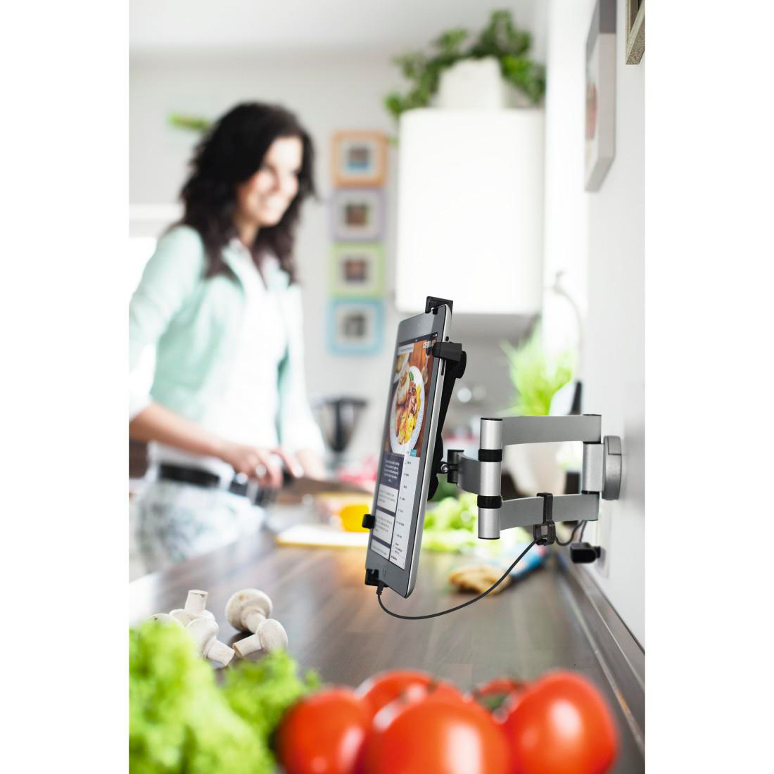 Ein Tablet an der Wand, das ein Rezept anzeigt. Im Hintergrund ist eine Frau zu sehen.