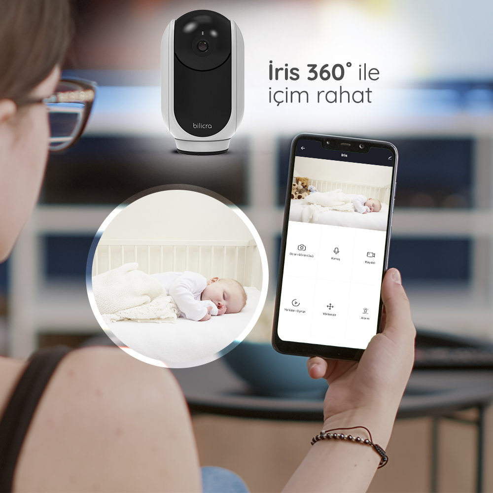Bir kadın, bebek monitörüyle telefonuna bakıyor. Bir bebek beşiğinde uyuyor.