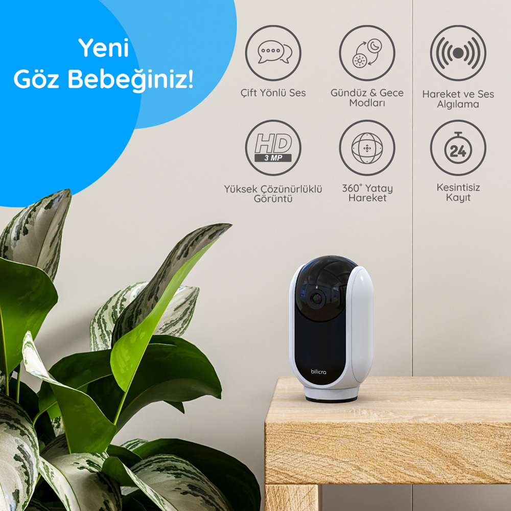 Beyaz ve siyah güvenlik kamerası, ahşap masada bitki yanında, simgeler ve metinlerle.