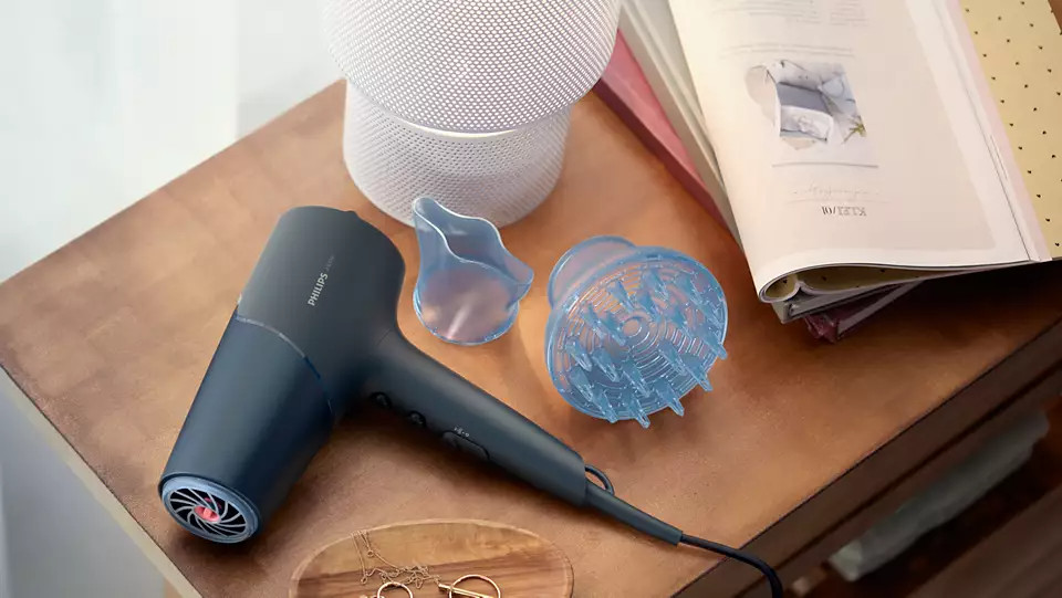 Hairdryer, diffuser, and styling nozzle on a wooden surface with a magazine.