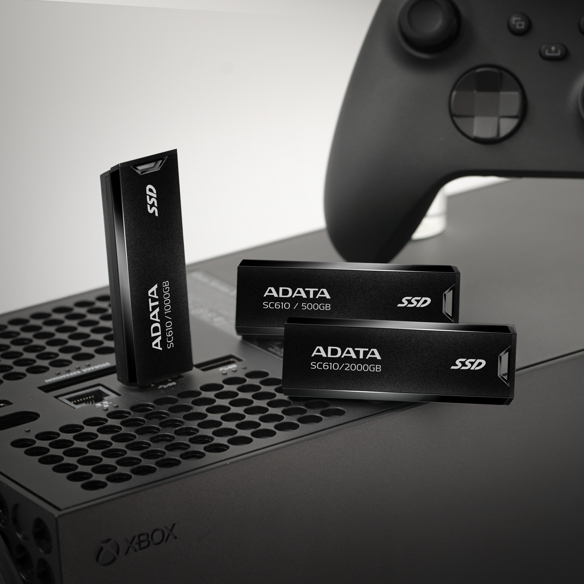 Három fekete SSD meghajtó egy Xbox konzolon. Egy álló, kettő fekvő. A márka ADATA.