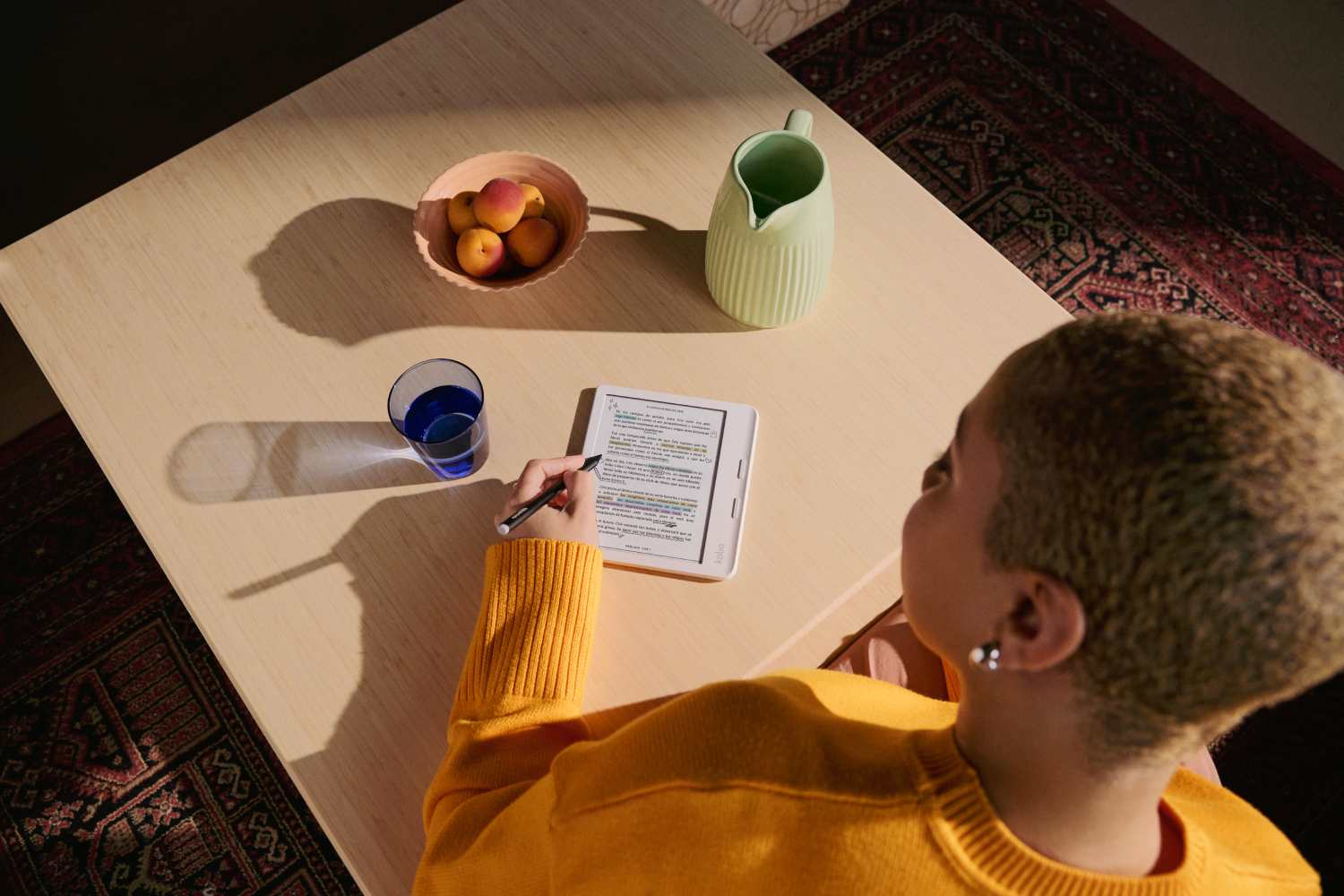 Una persona con cabello rubio leyendo en una tableta blanca sobre una mesa de madera.