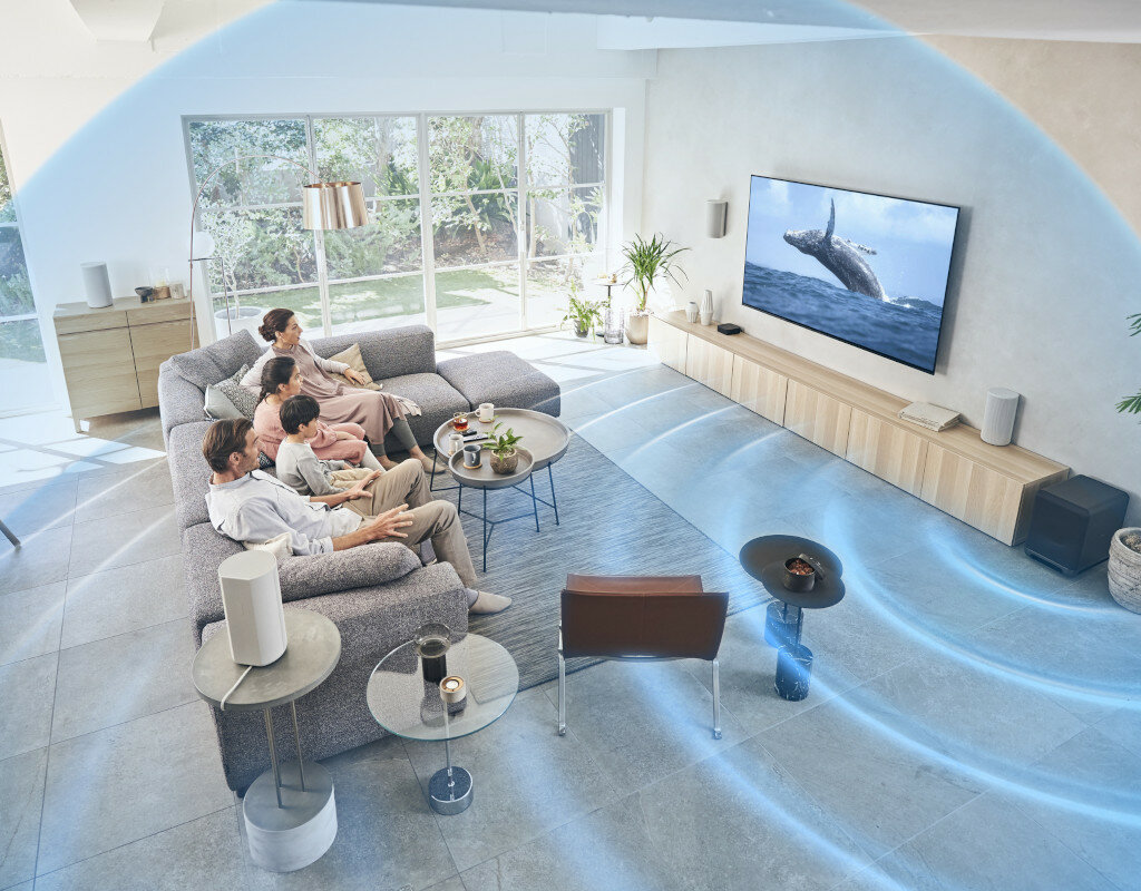 Salon z rodziną oglądającą telewizję. Wieloryb skacze na ekranie. Fale dźwiękowe są wizualizowane wokół ekranu.