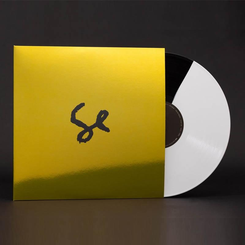 Gelbe Vinyl-Schallplattenhülle. Schwarzes Logo und eine weiße Schallplatte sichtbar.