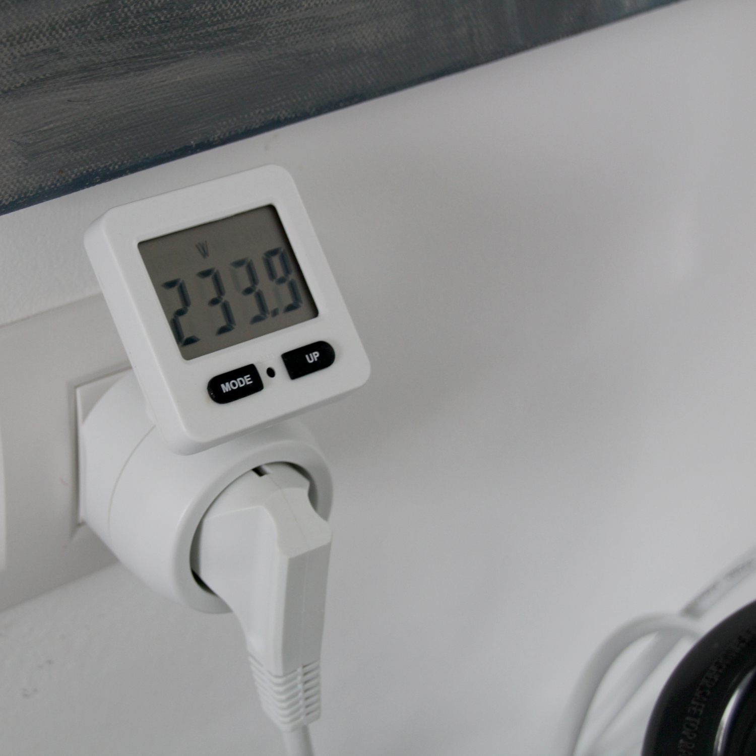 Un compteur d'énergie blanc branché dans une prise. Affiche la consommation en watts (233,9).