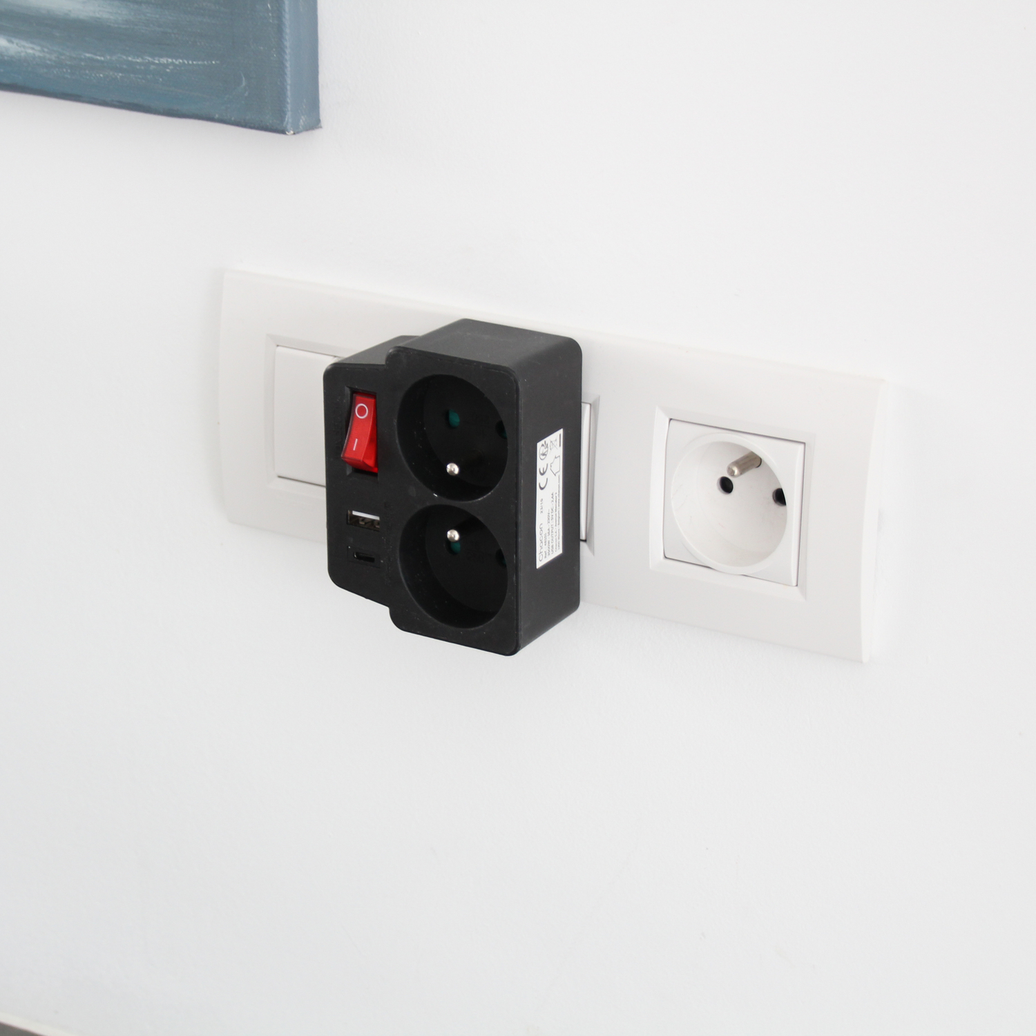 Adaptateur secteur noir branché dans une prise murale blanche, avec un interrupteur rouge.