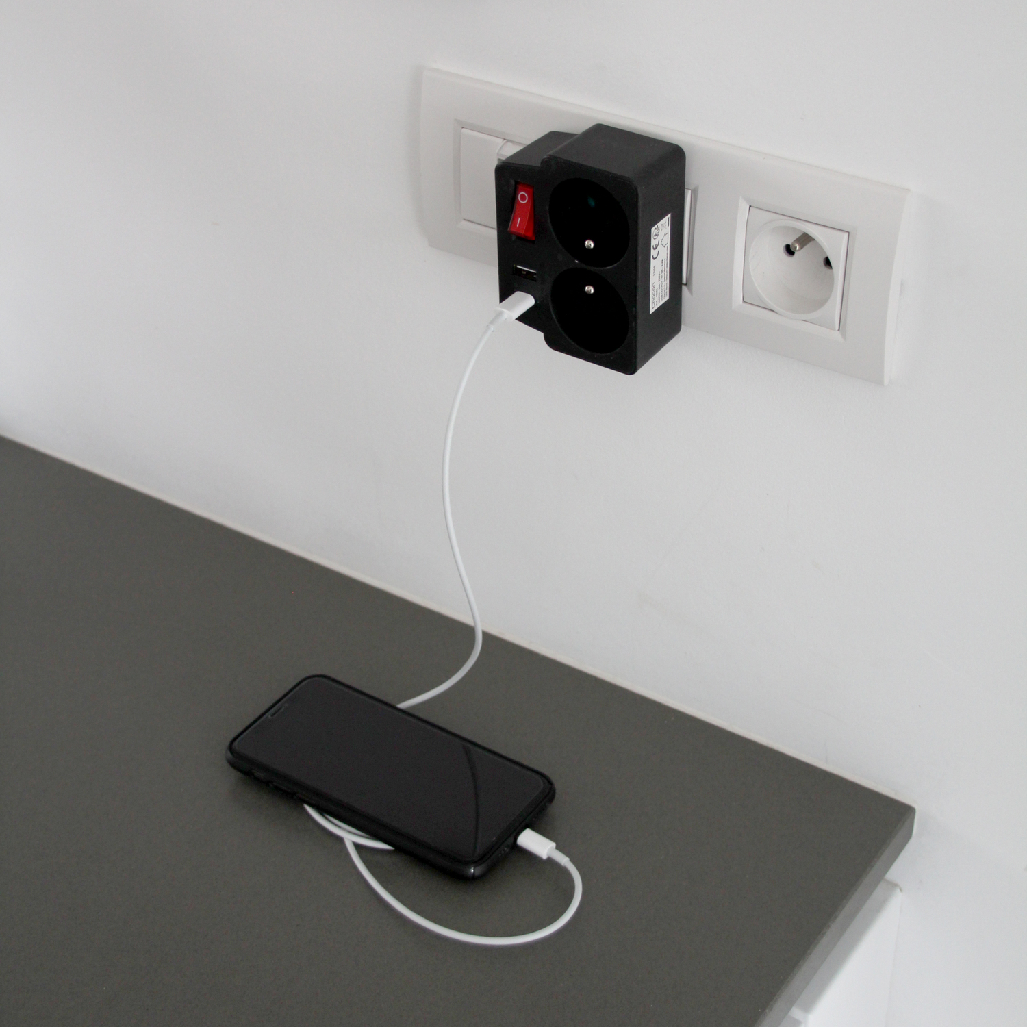Un téléphone en charge sur un comptoir à côté d'une prise et d'un adaptateur de charge.