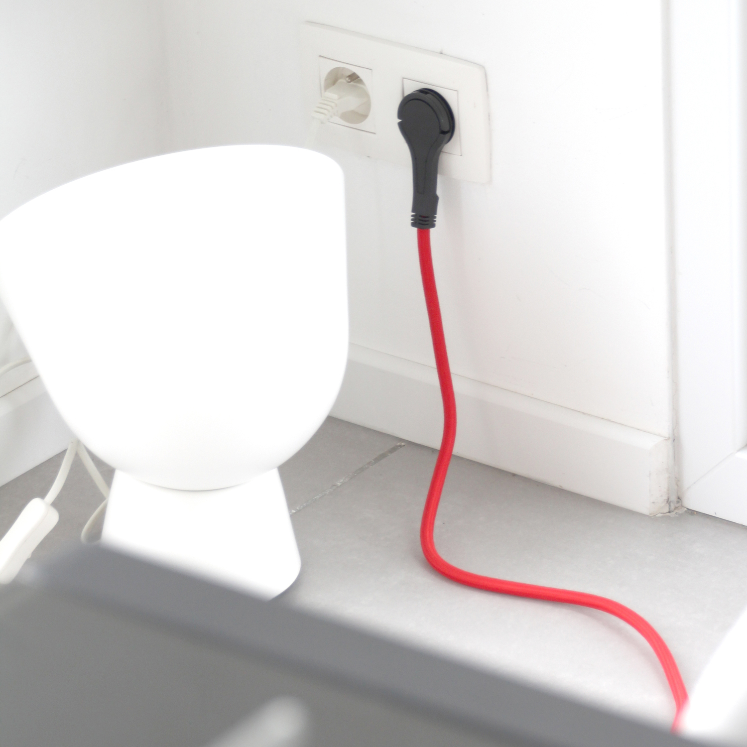Une prise blanche est dans une prise murale, avec un câble rouge.