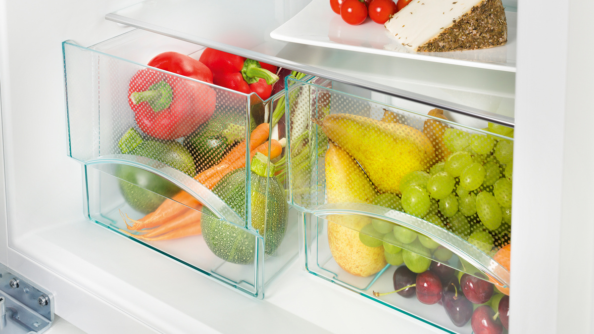 Kühlschrank Schublade voller frischem Gemüse und Obst, in weißem Innenraum.