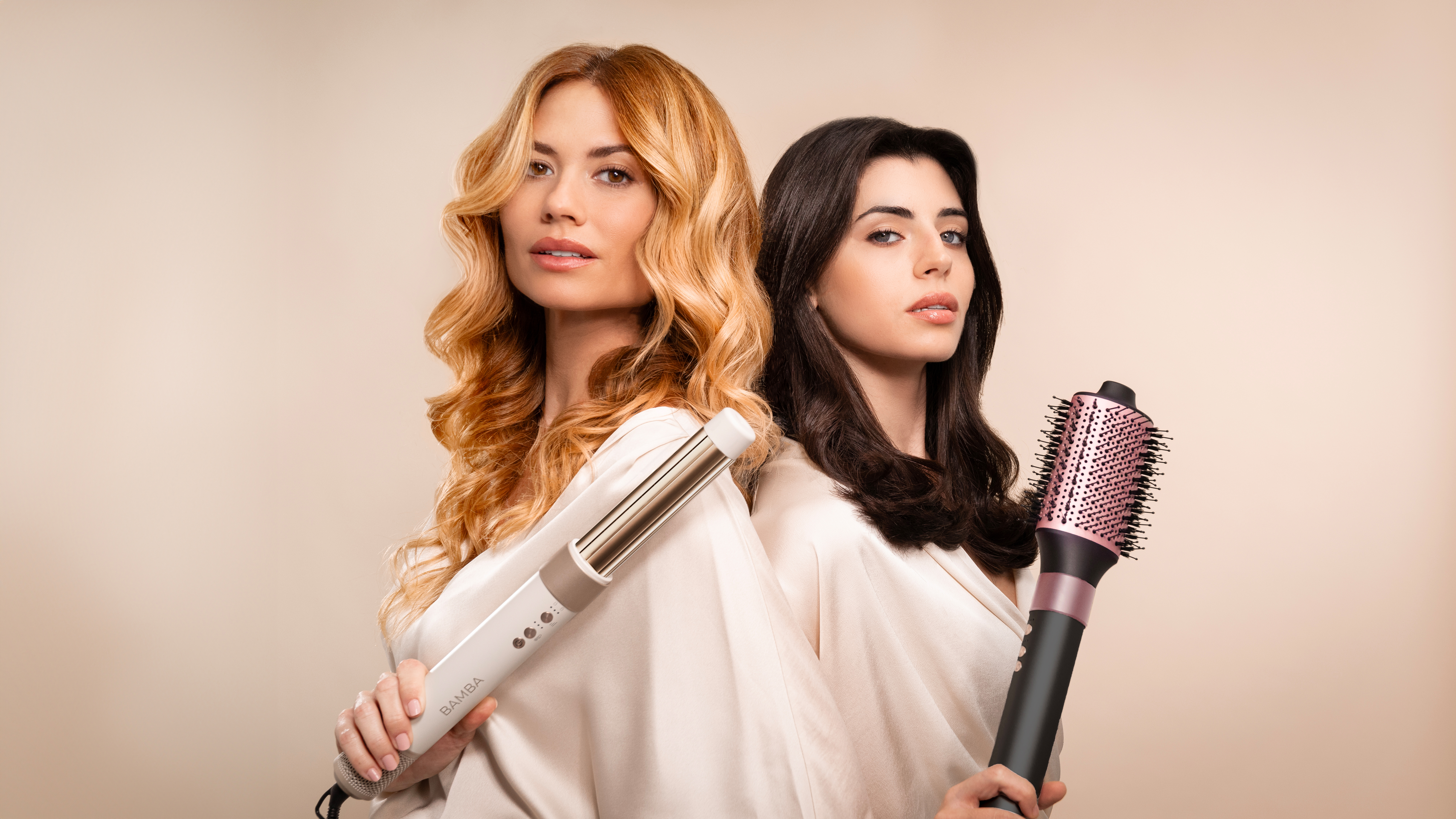Dos mujeres, una con rizos rubios, otra con cabello negro, sosteniendo herramientas de peinado.