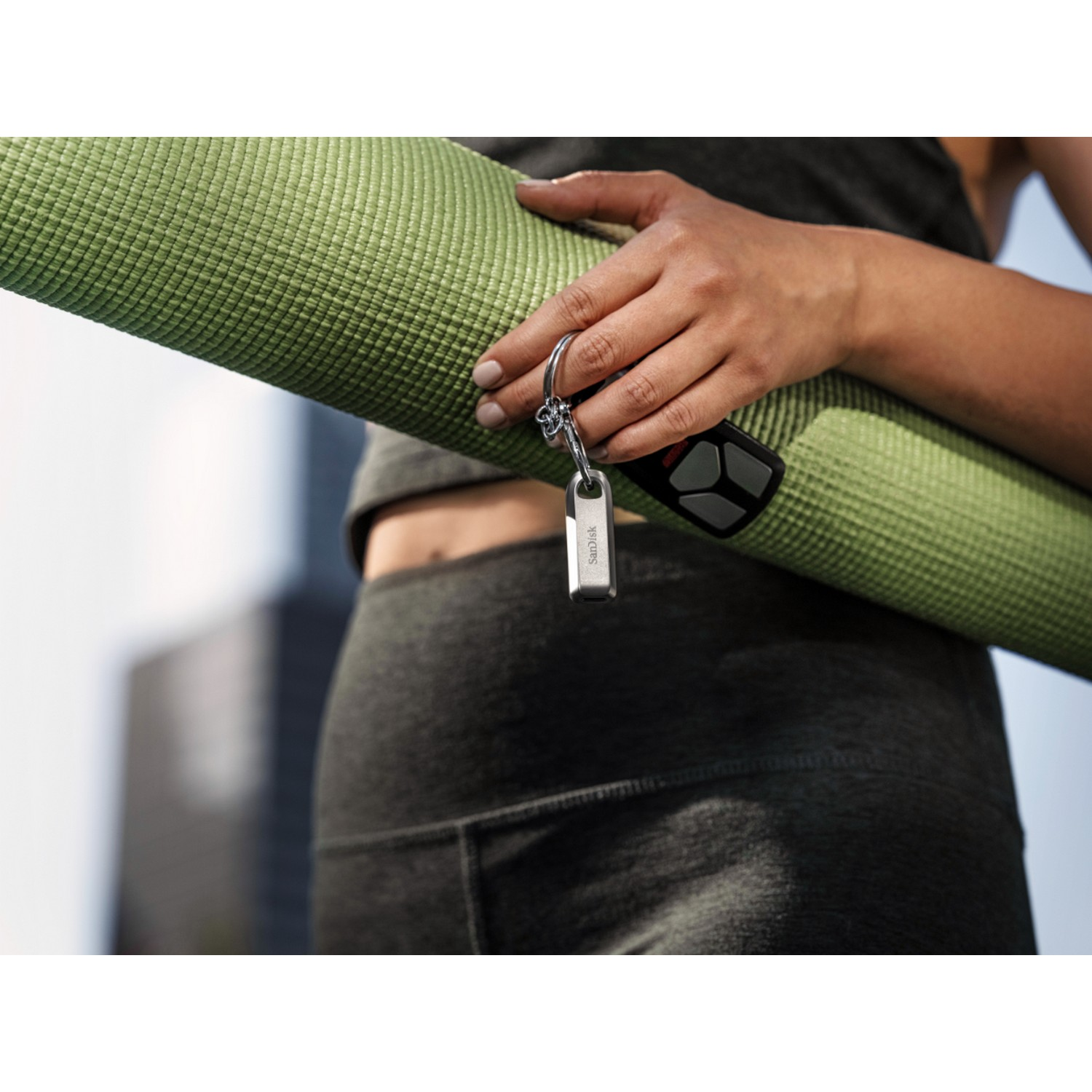 Una persona sostiene una esterilla de yoga verde y un llavero con una unidad USB y un mando a distancia.