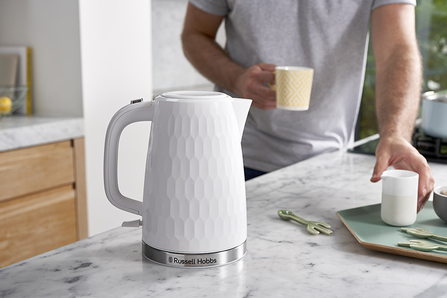 Fehér Russell Hobbs vízforraló pulton, személlyel és egyéb tárgyakkal.