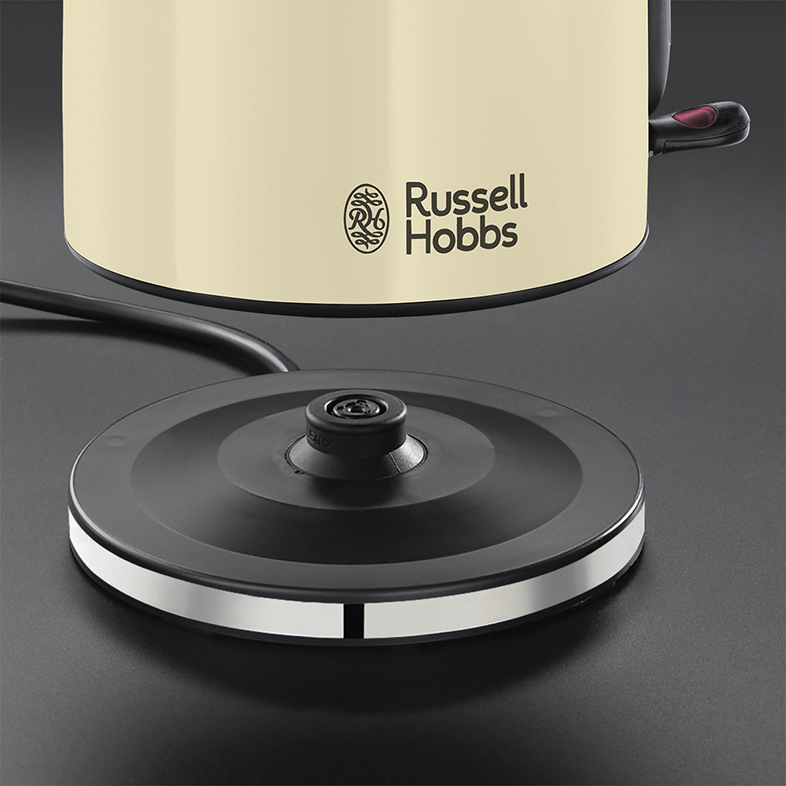 Krémszínű vízforraló fekete talpon, Russell Hobbs logó. Fényes fémcsík az alapon, fekete tápkábel.