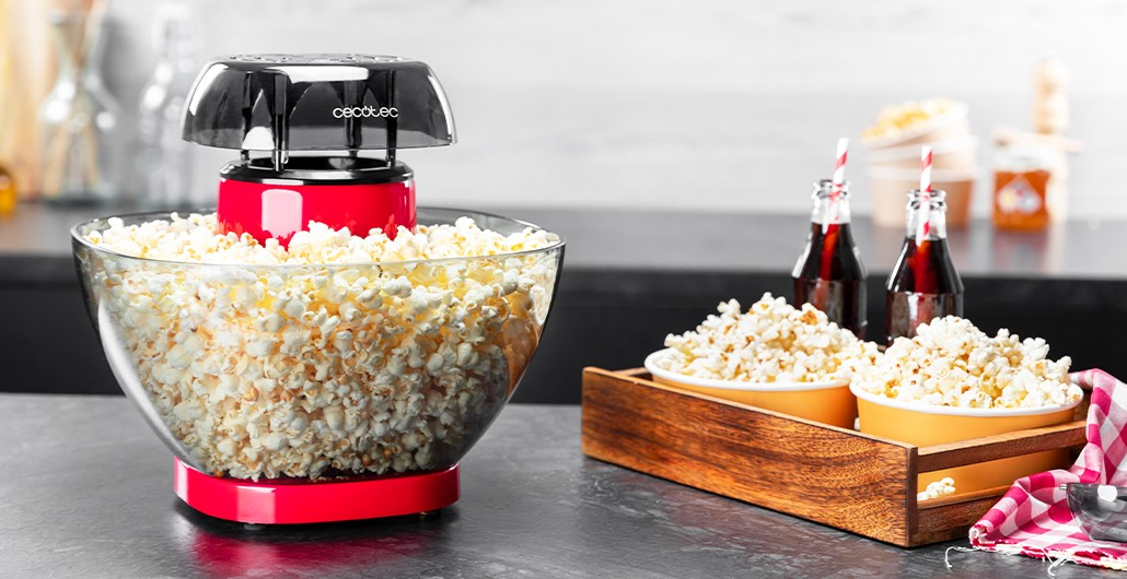 Una máquina de palomitas roja con un bol de palomitas y dos botellas de refresco en una encimera.