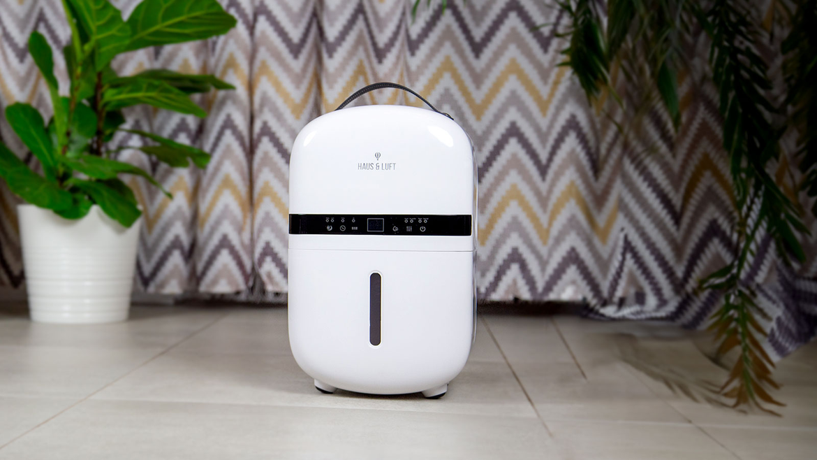 Biały osuszacz z uchwytem, przed zasłoną i roślinami na drewnianej podłodze.