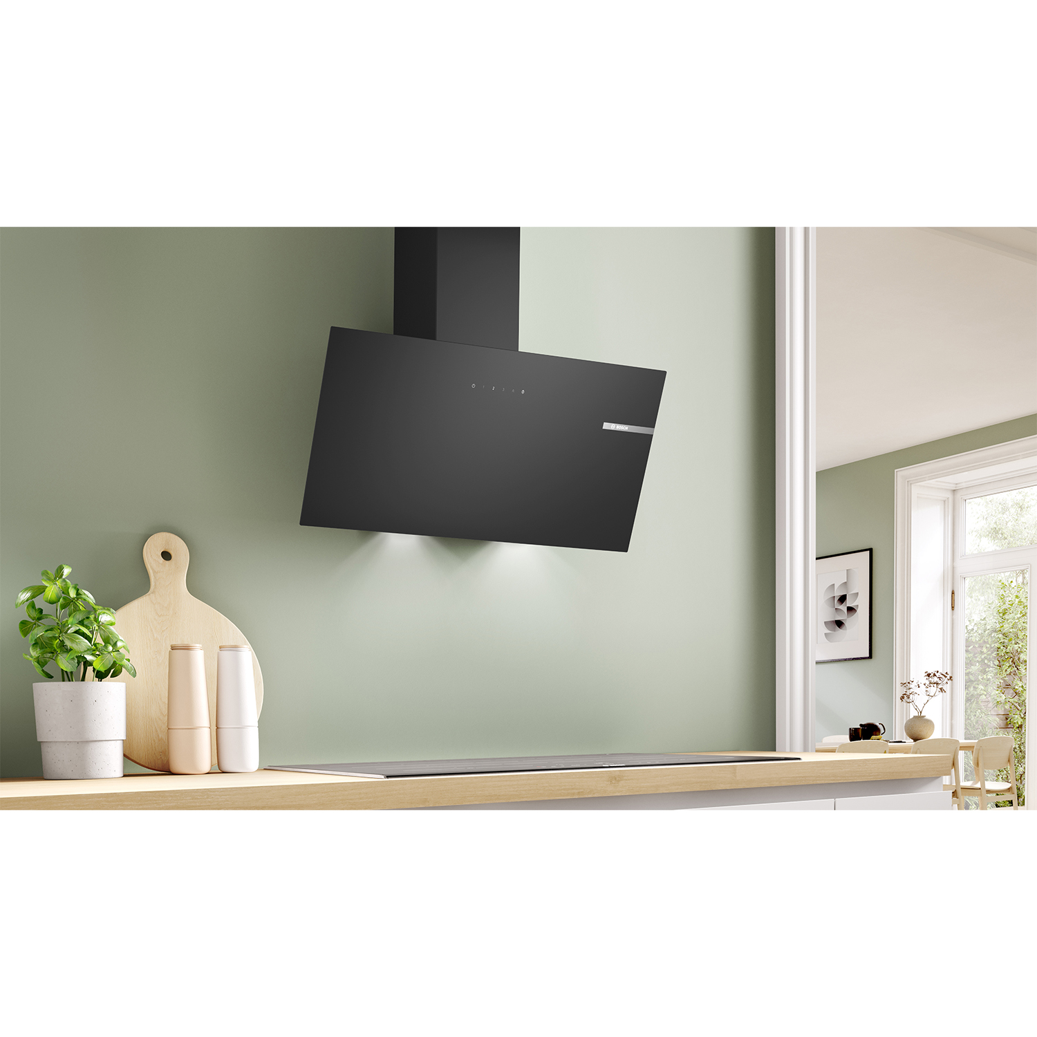 Scena cucina con cappa nera sopra un piano cottura a induzione. Parete verde e superficie in legno.