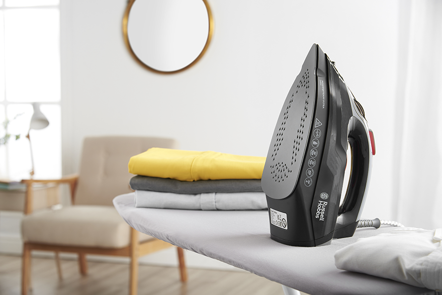 Fekete vasaló ruhákkal a vasalódeszkán, háttérben tükör és szék.