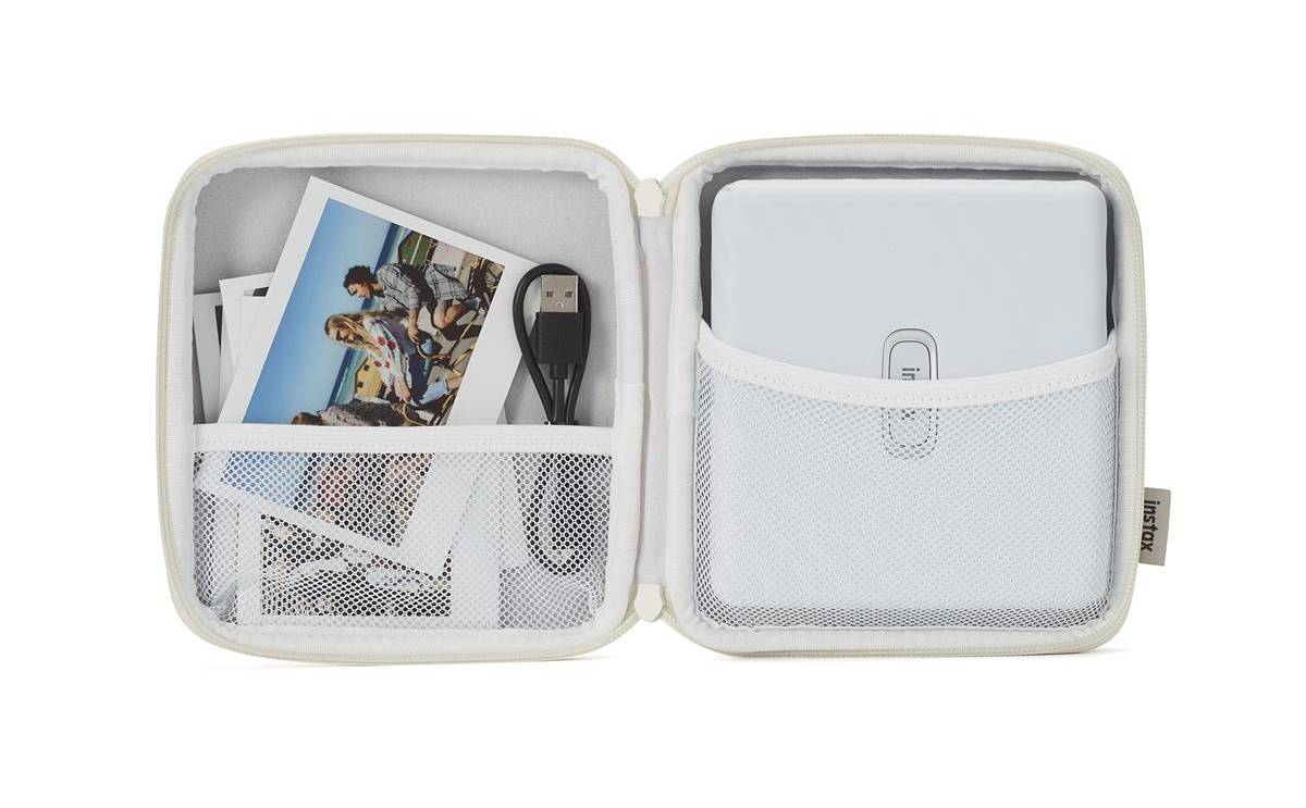 Estuche abierto, mostrando cámara Instax, fotos y cable USB. Estuche blanco y gris.