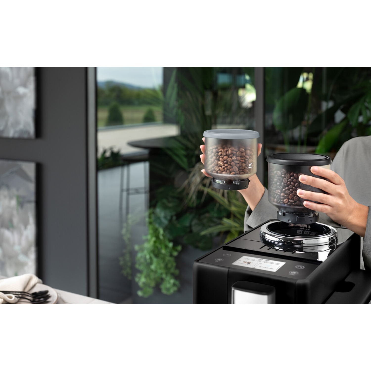 Person holding two containers of coffee beans for a coffee machine.