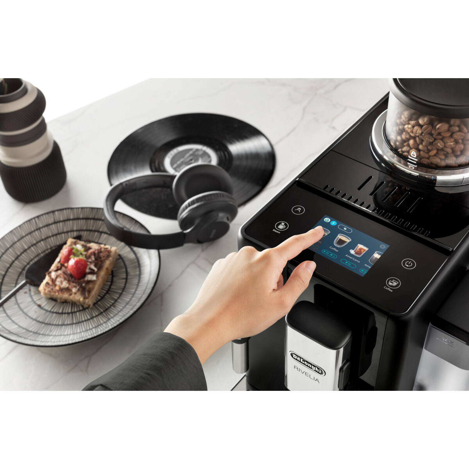 Een hand wijst naar het touchscreen van een koffiezetapparaat met eten en een koptelefoon.