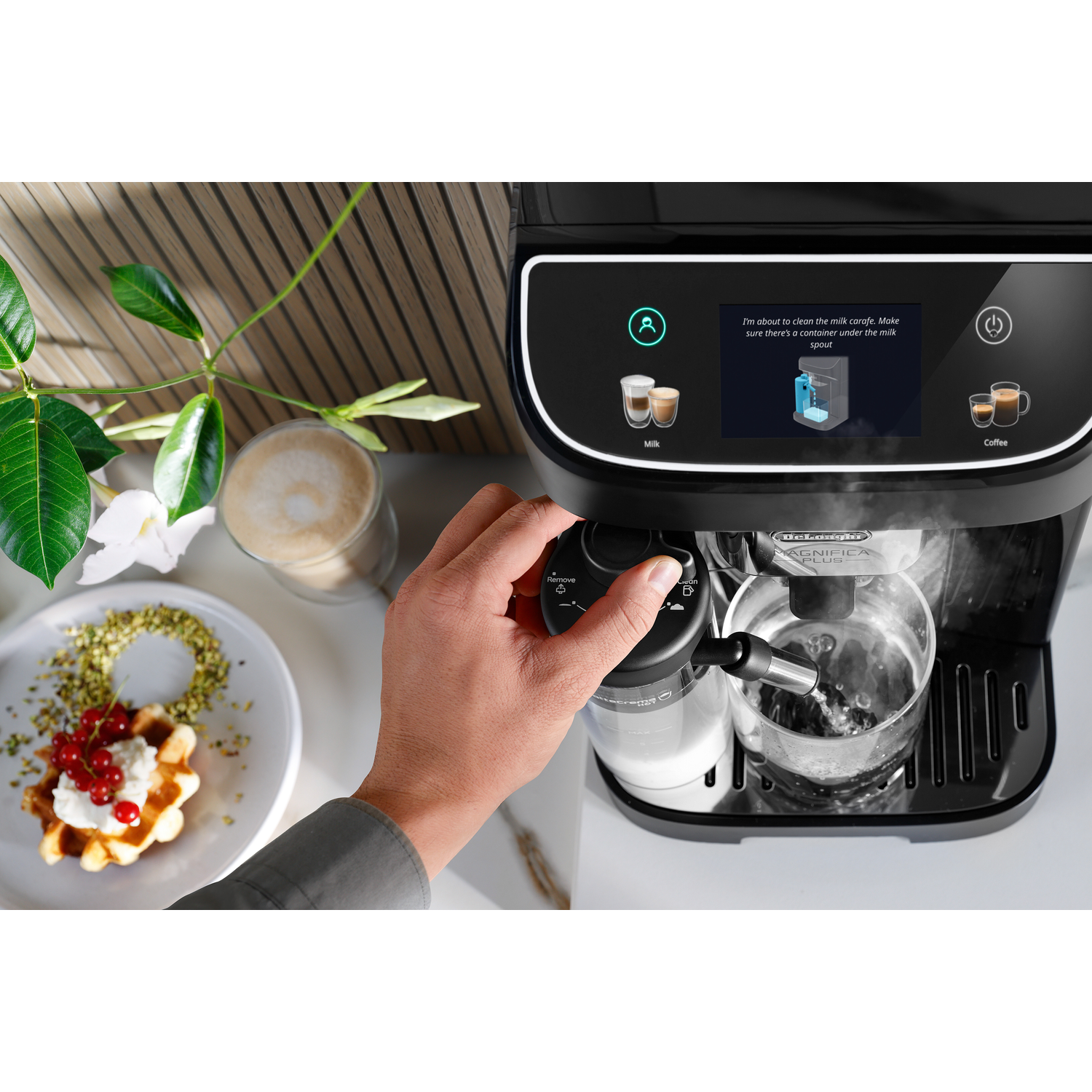 Een persoon gebruikt een De'Longhi koffiemachine. Het display toont instructies en een glas vult zich met water.