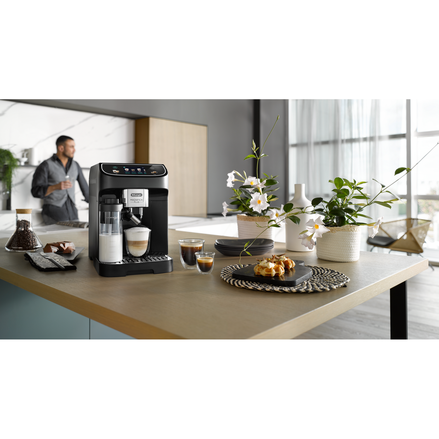 Een zwarte koffiemachine, met kopjes en melkopschuimer, op een houten tafel.