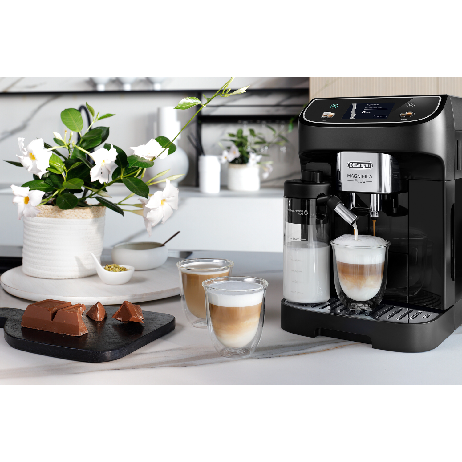 Een zwarte koffiemachine met melk, twee glazen koffie en een chocoladereep.