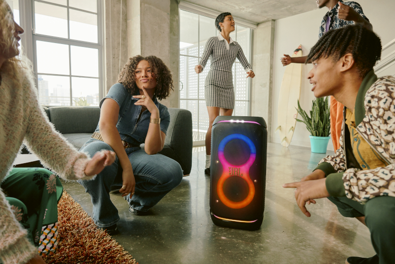 Grupa osób wokół głośnika, tańcząca i wchodząca w interakcje.