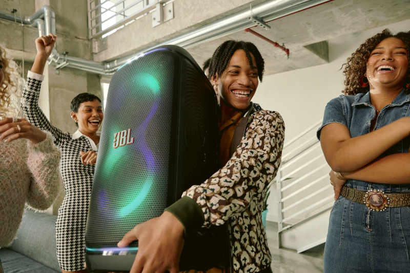 Ludzie z dużym, czarnym głośnikiem JBL. Głośnik ma kolorowe światła.