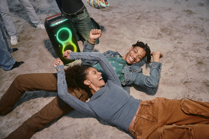 Dwie osoby tańczące w pobliżu głośnika przenośnego na plaży w nocy.