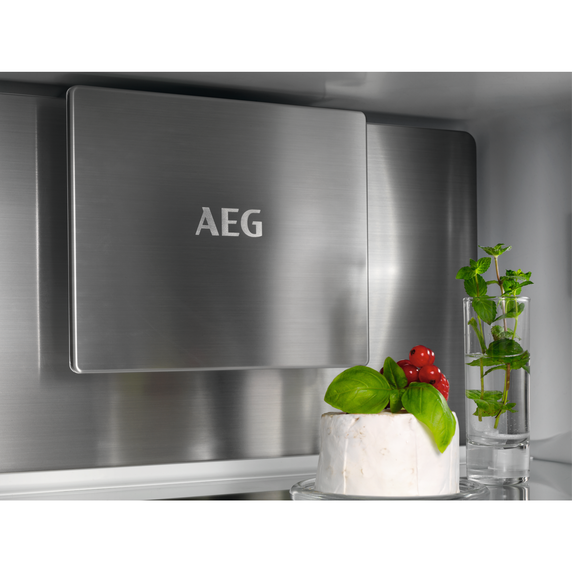 Im Kühlschrank: Edelstahlplatte mit 'AEG'-Logo, Käse, Beeren und Kräuter im Glas.