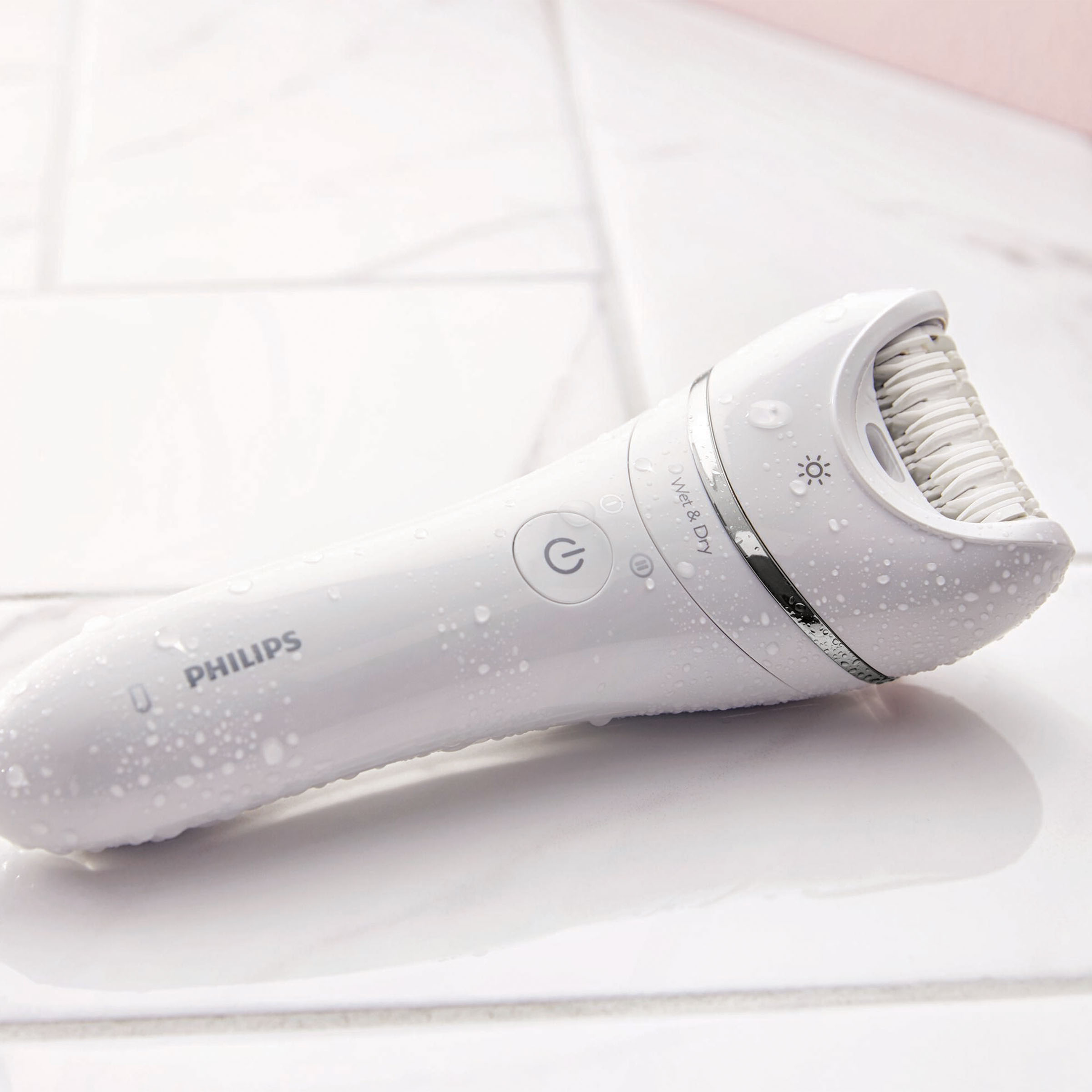 Biały depilator Philips na kafelkowej powierzchni, z widocznymi kroplami wody.