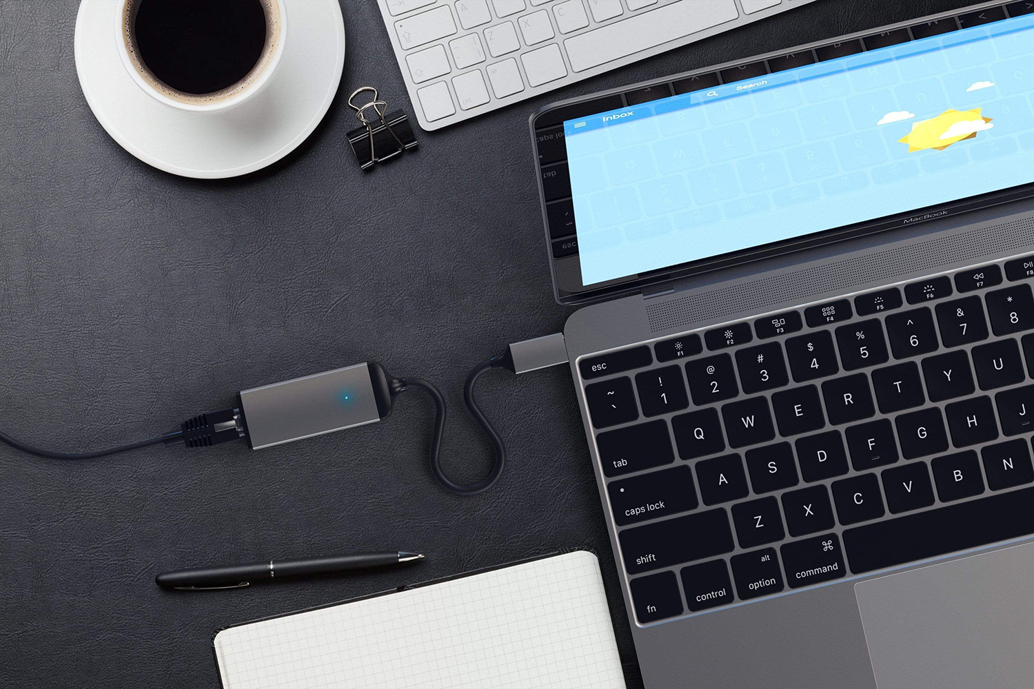 Laptop egy szürke adapterhez csatlakoztatva, egy kávéscsészével.