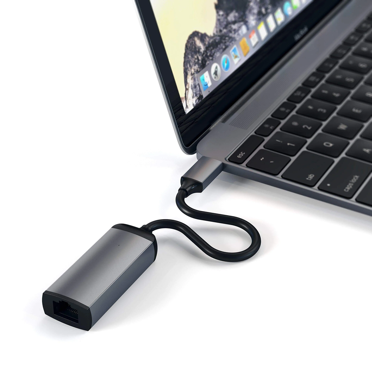 Laptop szürke adapterhez csatlakozik fekete kábellel, fehér felületen.