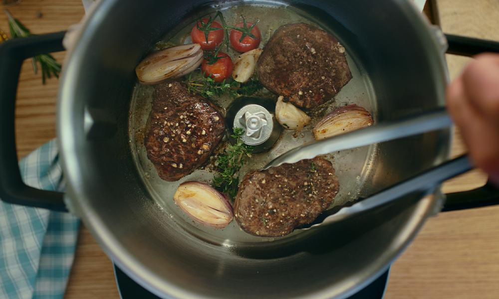 Kochen in einem Topf mit Fleisch, Gemüse und Zangen.