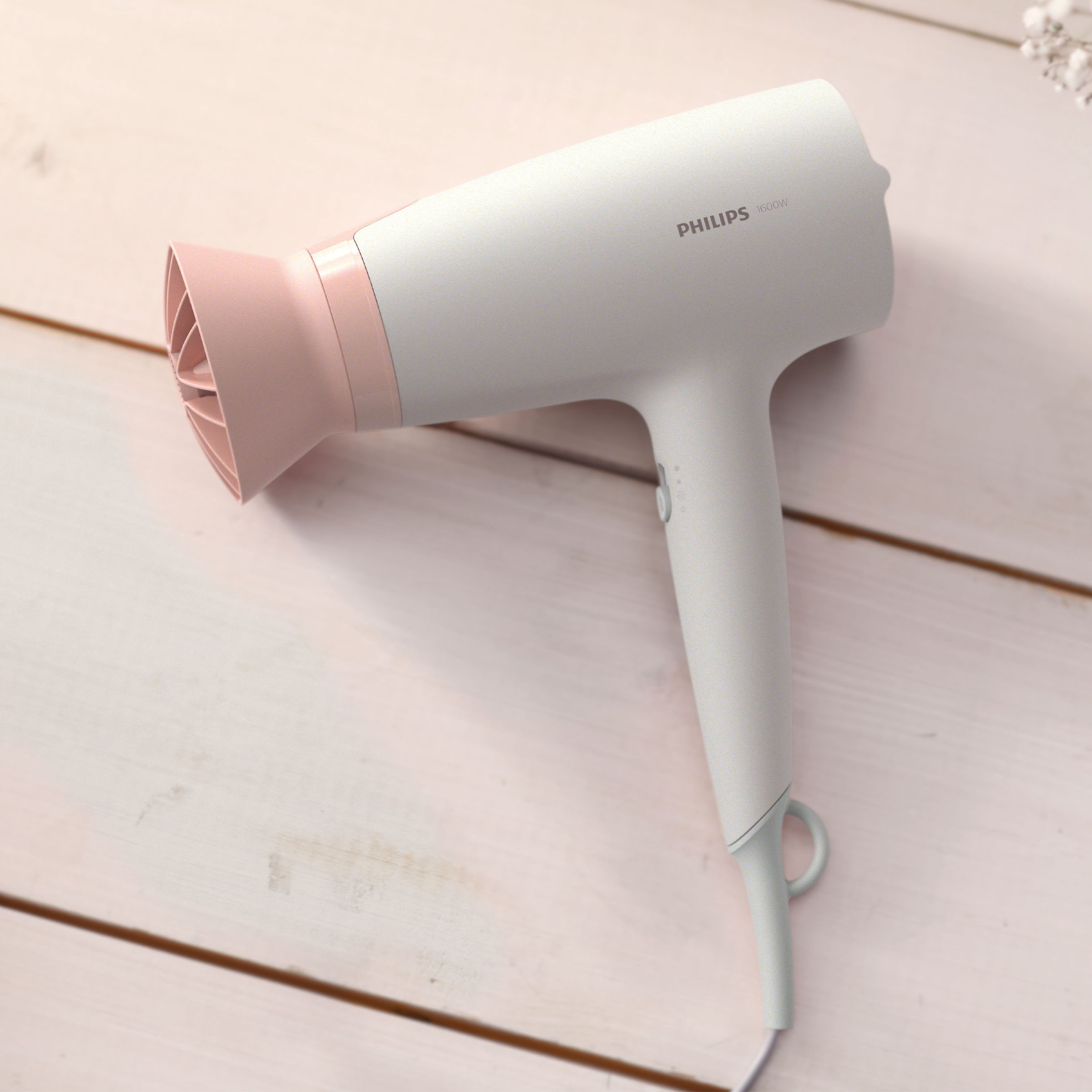 Biała i różowa suszarka do włosów Philips na jasnej drewnianej powierzchni. Logo jest widoczne.