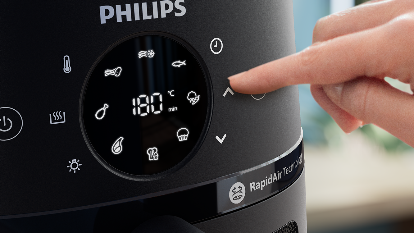 Egy személy ujja megnyom egy gombot a fekete Philips Airfryer vezérlőpanelen.