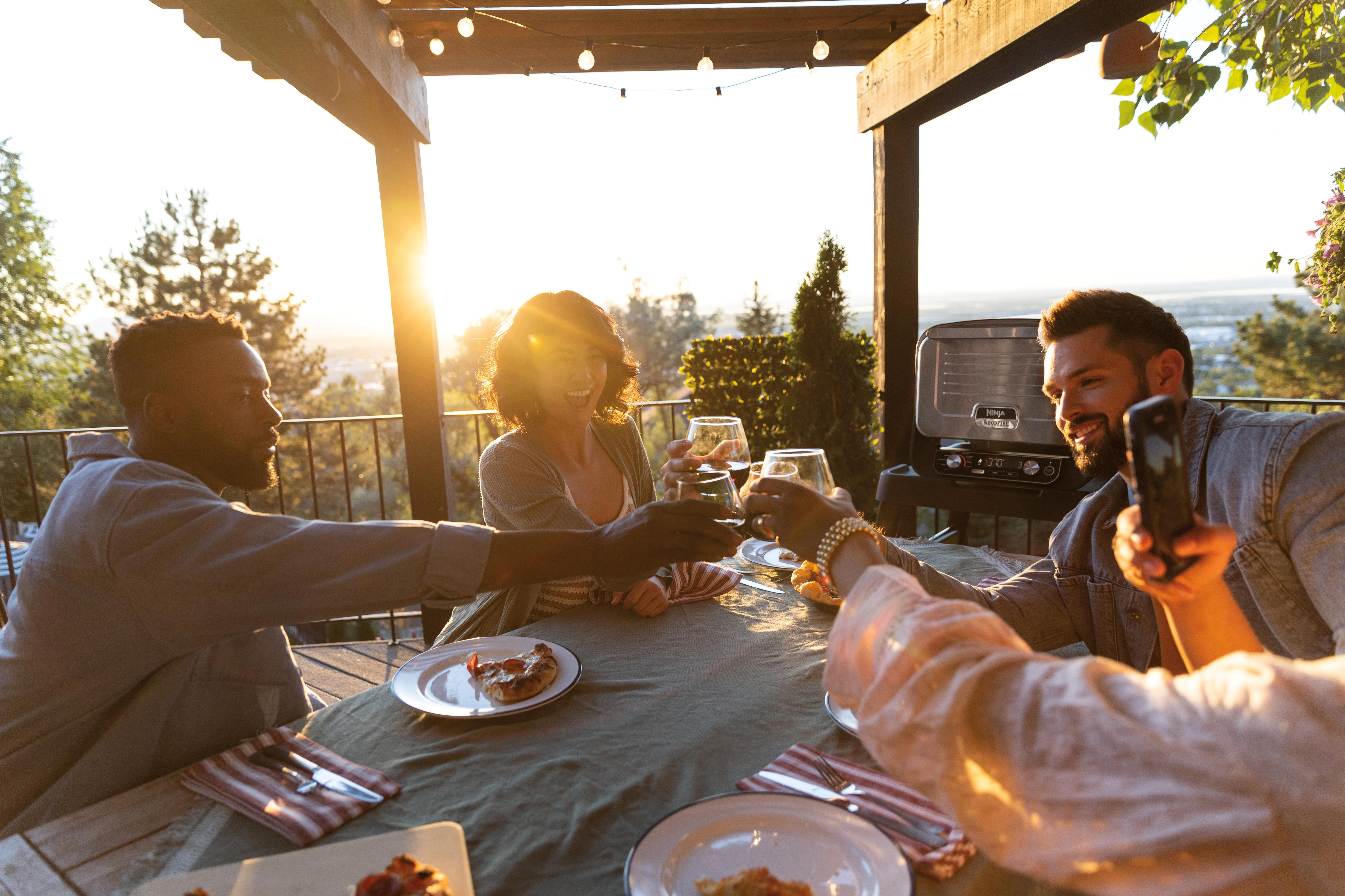 Gruppe von Leuten, die draußen an einem Tisch mit Wein anstoßen.