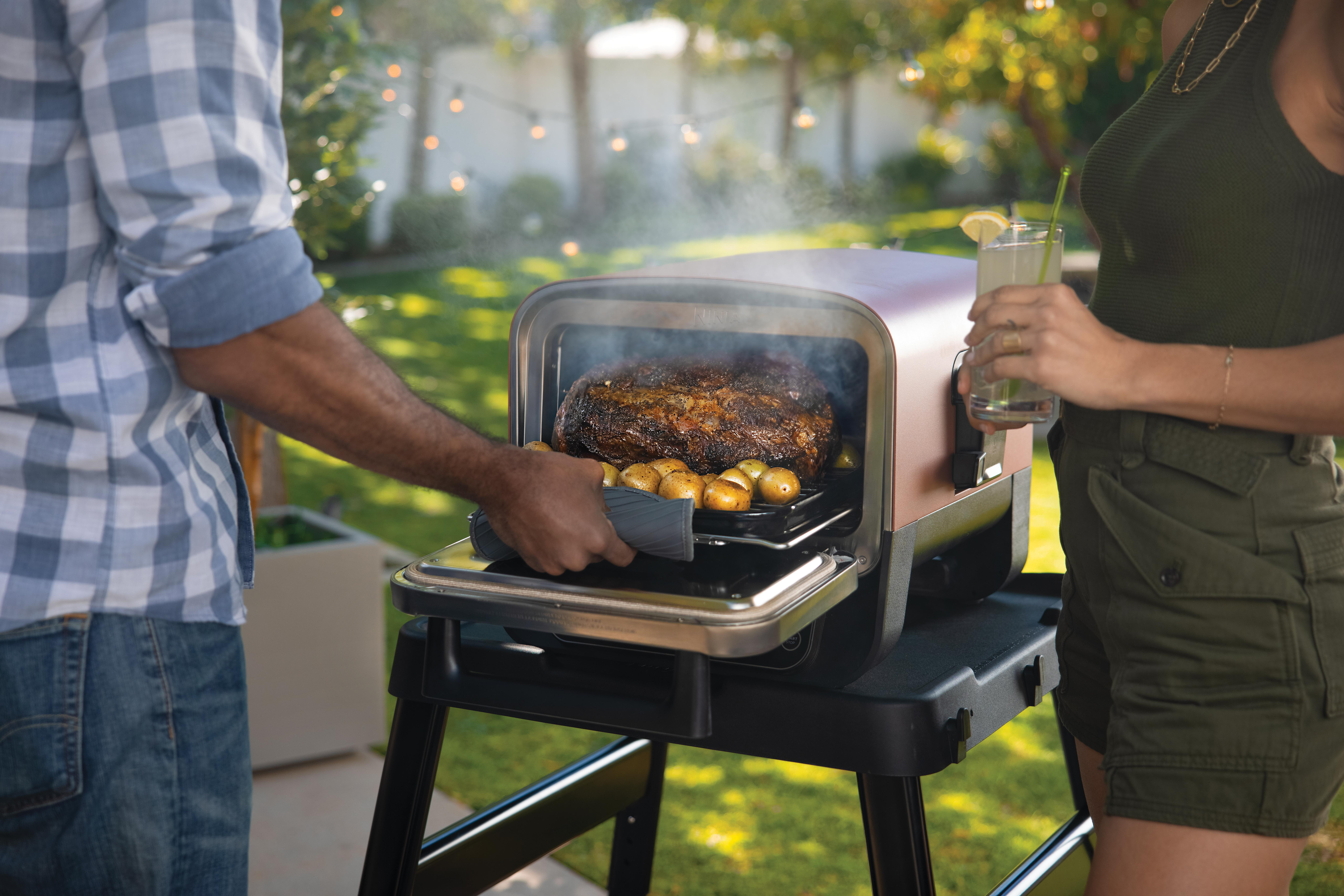 Leute kochen draußen mit Grill. Mann legt Essen in den Grill. Frau hält Getränk.