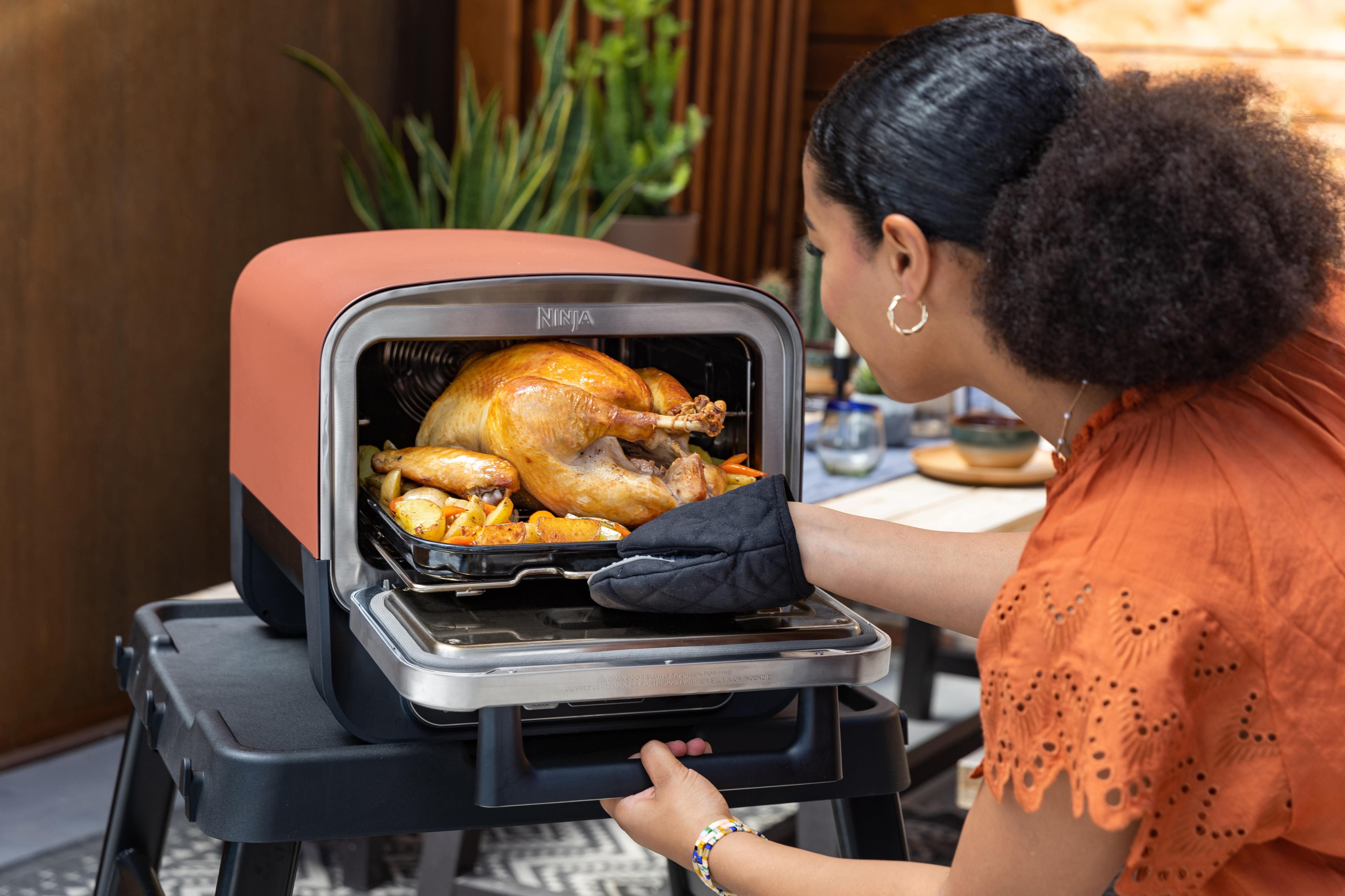 Frau, die einen gekochten Truthahn aus einem roten Ofen auf einer schwarzen Oberfläche nimmt.