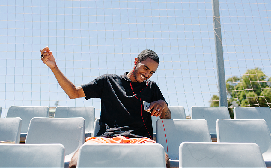 Uomo sorridente in una seduta dello stadio che ascolta musica sul suo telefono.
