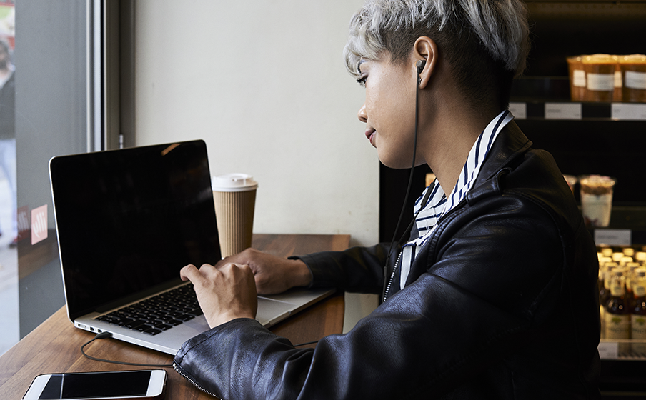 Una persona sta lavorando su un laptop in un bar, con una tazza e un telefono.