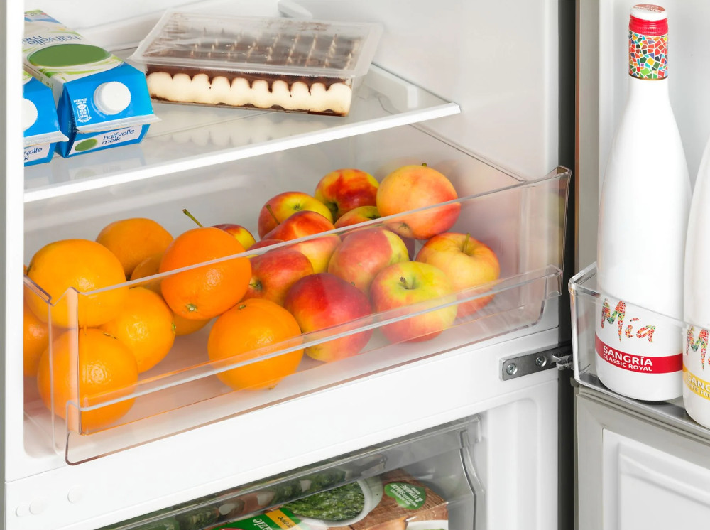 Intérieur du réfrigérateur avec fruits, desserts et boissons. Étagères et tiroirs transparents.