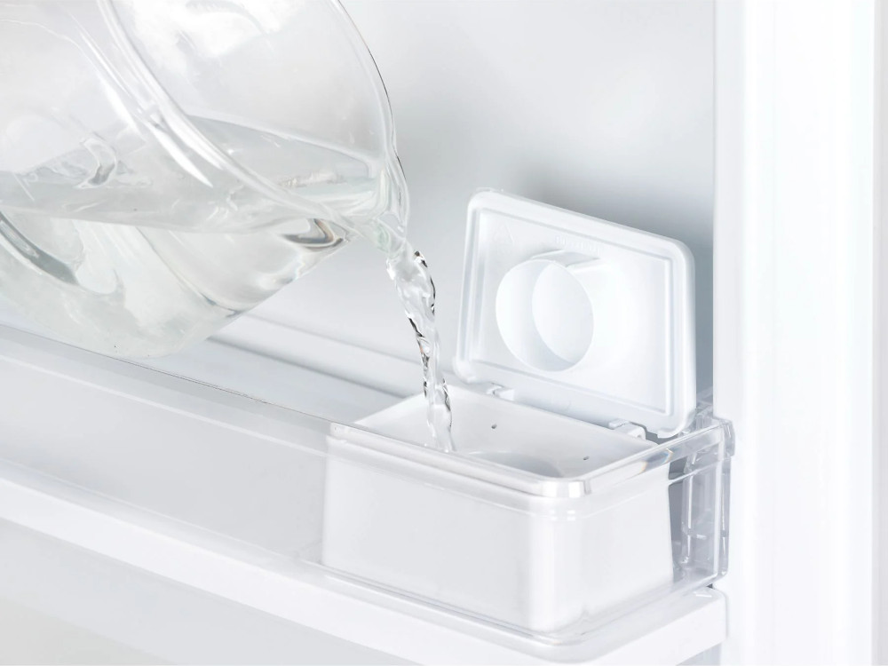 De l'eau versée d'une carafe dans un récipient blanc à l'intérieur d'un frigo.