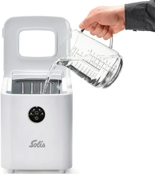 Une machine à glaçons blanche avec de l'eau versée dedans à partir d'une carafe en verre.